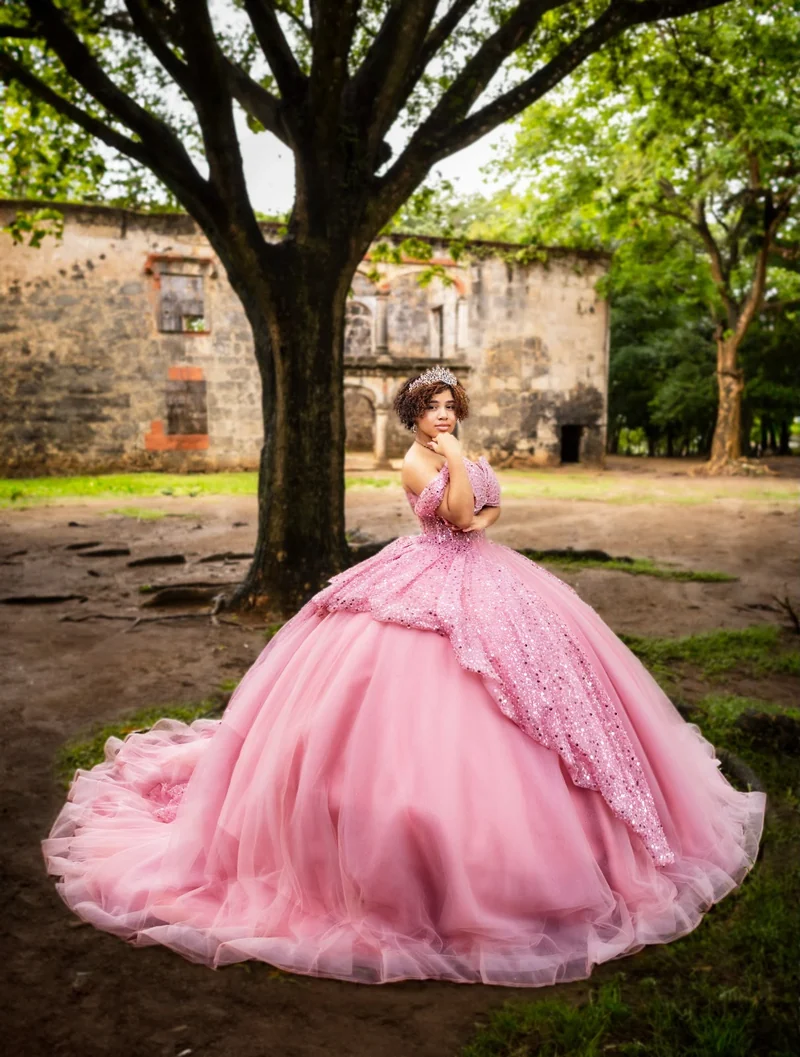 Retrato con vestido rosado entre árboles y muros de piedra.